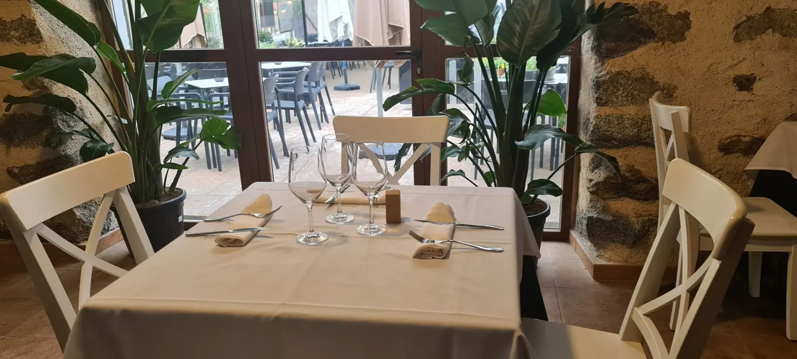 Salón de VACAMU con muros de piedra, mesas vestidas y la terraza al otro lado del ventanal